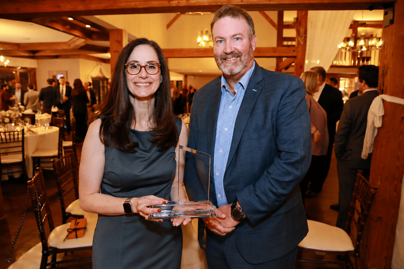 Couple posing with an award at a formal event, surrounded by elegantly set tables and guests in the background.